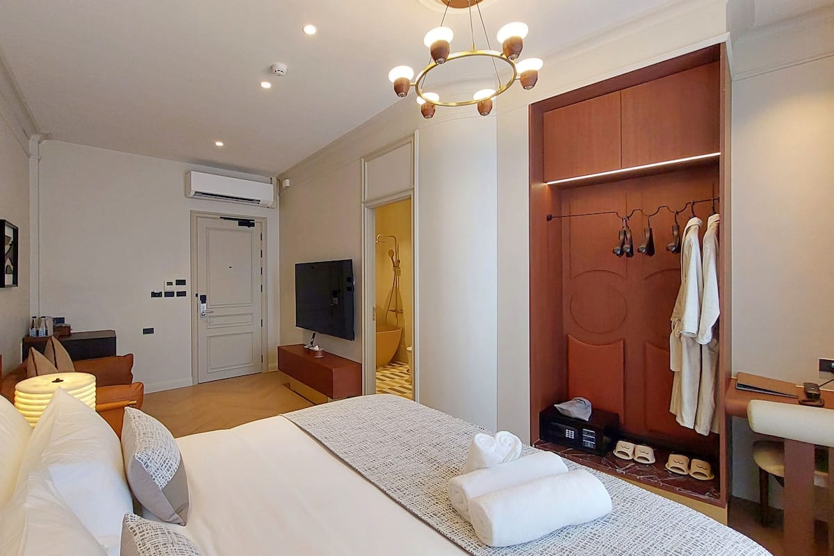 A hotel room with a bed, bedside tables, a TV, a wardrobe, and a bathroom with a shower.
