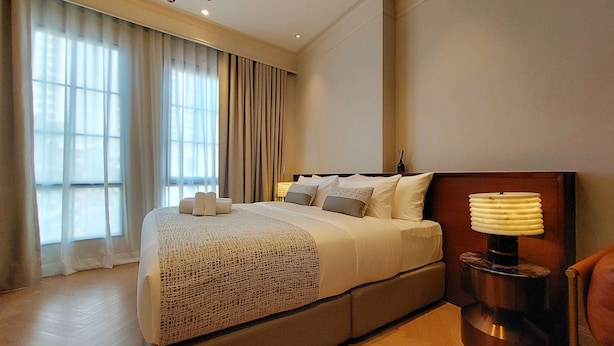 Ein Hotelzimmer mit einem großen Bett, einem Nachttisch mit Lampe und einem Fenster mit Vorhängen.