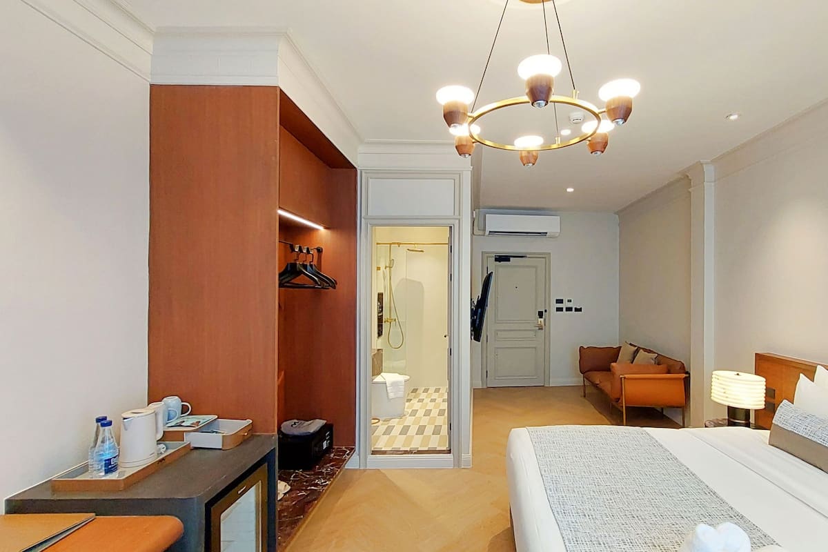 A hotel room with a bed, bedside table, chair, and a shower area.