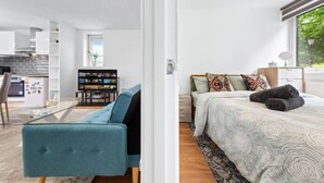 En modern lägenhet med ett vardagsrum som inrymmer en soffa, en tv och ett kök i bakgrunden.