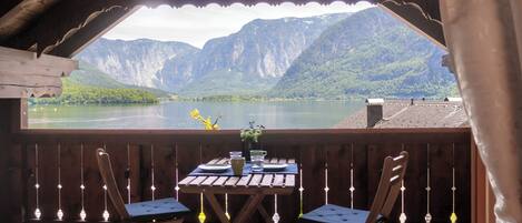 Una terraza de madera con una mesa y sillas con vista a un lago y montañas al fondo.