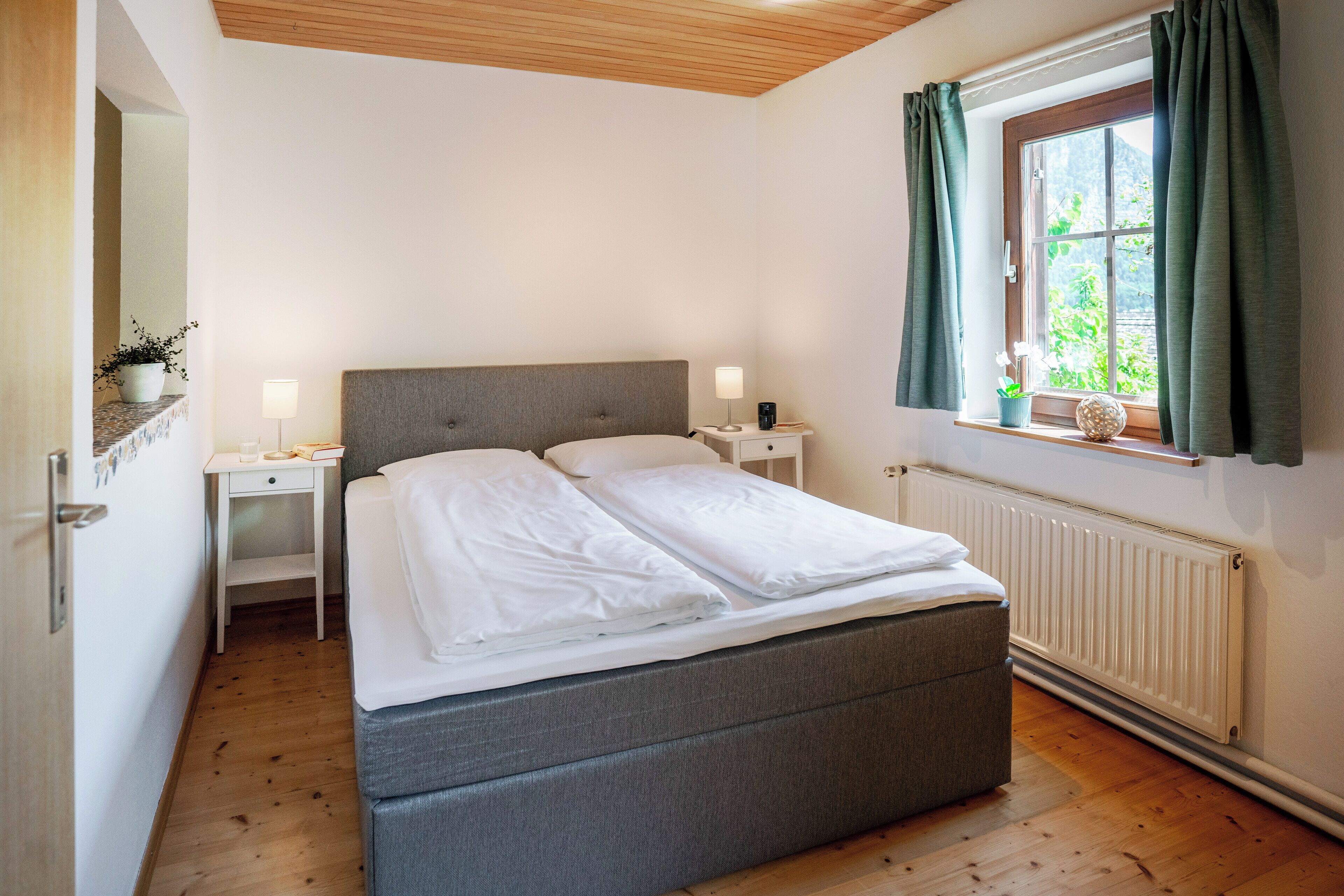 A neatly arranged bedroom with a bed, bedside tables, a window with curtains, and a radiator.