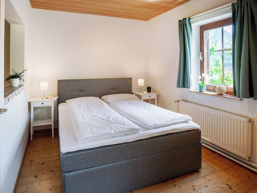 A neatly arranged bedroom with a bed, bedside tables, a window with curtains, and a radiator.