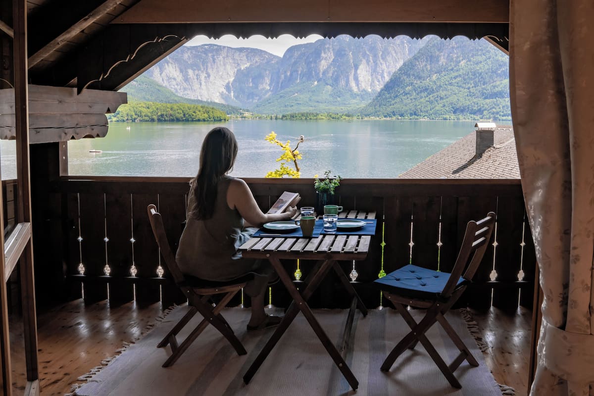 A wooden deck with a table and chairs overlooking a lake and mountains.