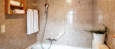 Un baño moderno con bañera, ducha y un estante de madera con toallas y artículos de aseo.