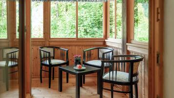 Una habitación con paneles de madera, una mesa y cuatro sillas, ventanas amplias y vistas al verdor exterior.