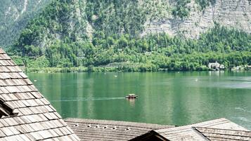 A view of a lake with a boat, surrounded by forested mountains and a building with a sloped roof.