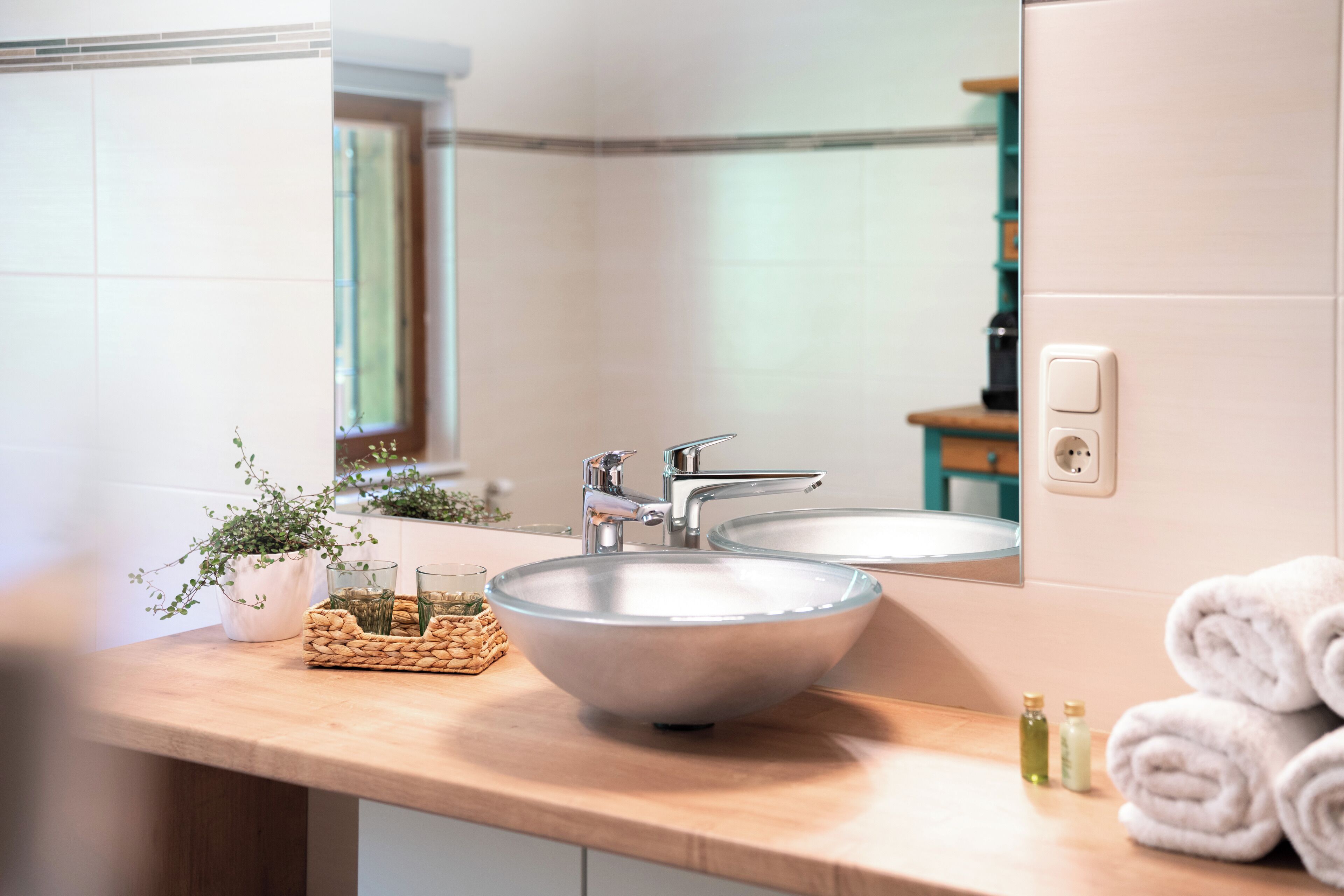 A bathroom with a large vessel sink, two mirrors, a towel rack, and a small plant.