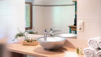 Une salle de bain avec un grand lavabo sur colonne, deux miroirs, un porte-serviettes et une petite plante.