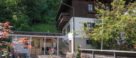 A wooden chalet with a balcony, outdoor seating, and a staircase leading to an upper floor.