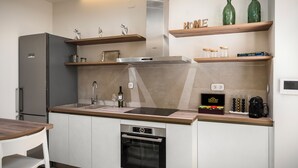 Une cuisine moderne dotée d’un four encastré, d’un réfrigérateur en acier inoxydable et d’étagères en bois ornées d’objets décoratifs.