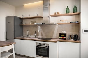 Una cucina moderna con forno a incasso, frigorifero in acciaio inossidabile e mensole in legno con oggetti decorativi.