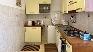 A compact kitchen with yellow cabinets, a small refrigerator, a gas stove, and basic appliances. - Paint House (Imperia)