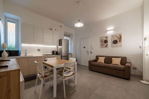 A modern kitchen with white cabinets, a dining table with chairs, a brown sofa, and abstract wall art.