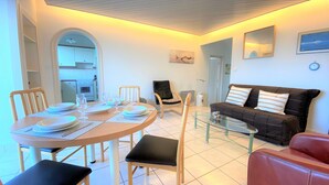 Un comedor con una mesa redonda preparada para cuatro personas, un sofá negro y una mesa de centro de vidrio.