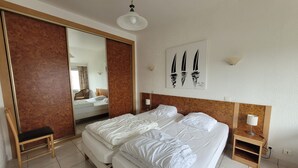 Habitación de hotel con una cama grande, cabecera de madera, mesita de noche con lámpara, espejo y un cuadro de veleros.