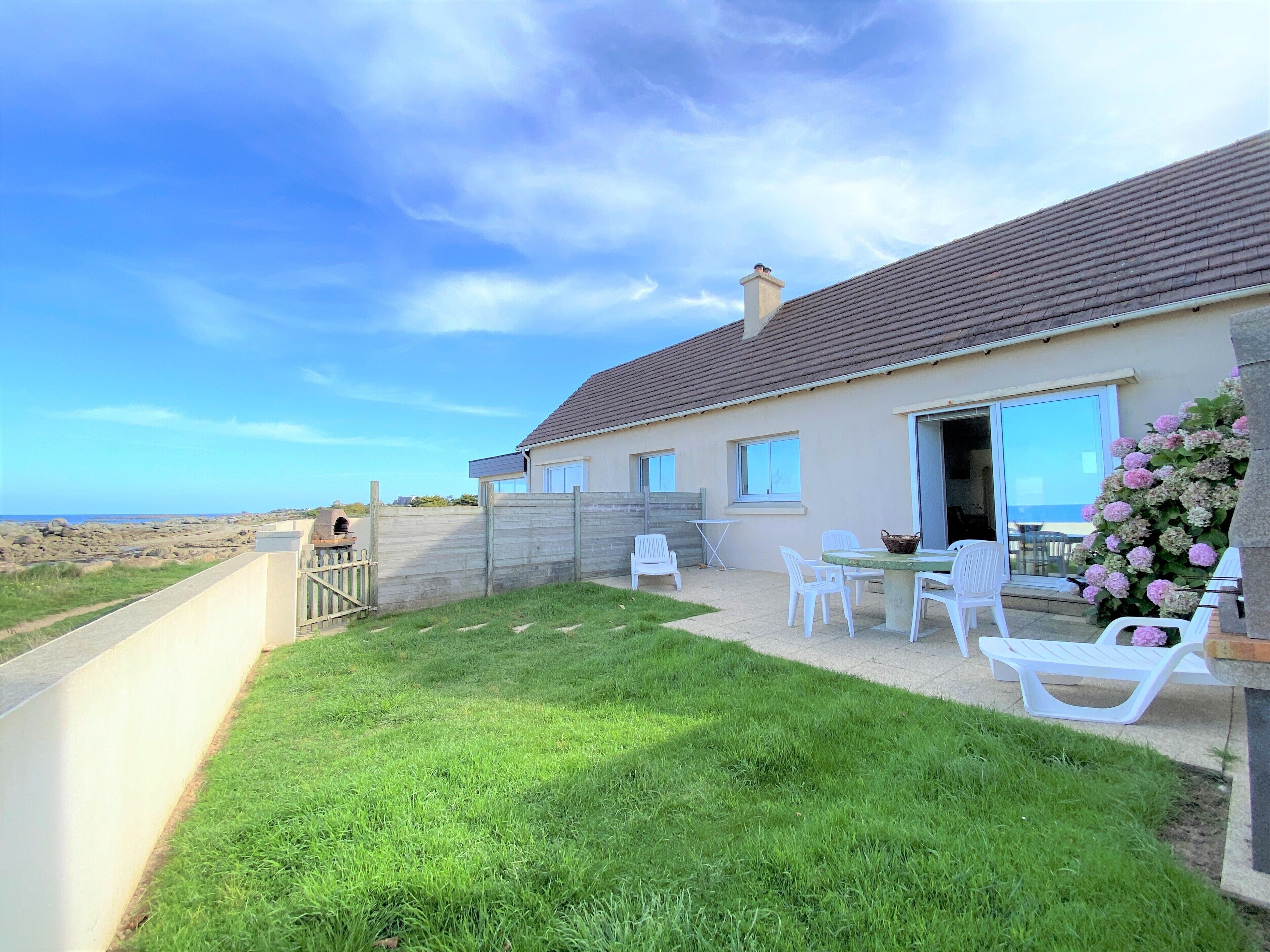 A house with a patio, white chairs, and a view of the sea.
