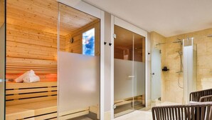 A modern bathroom with a sauna, glass shower enclosure, and a wooden bench with towels. - Dünenloft, House Kliff Whg. 11 - Dünenlofts (Sylt)