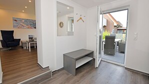 Et moderne interiør med en bænk, en stol og et spiseområde, der kan anes gennem en åben dør.