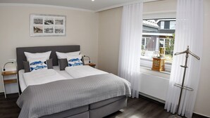 A modern bedroom with a large bed, a bedside table, a nightstand, a framed picture on the wall, and a window with curtains. - Island Feeling Apartment 2 (Büsum)