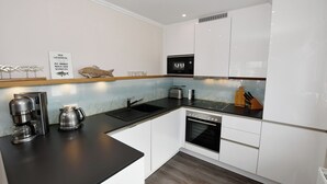 A modern kitchen with white cabinets, a black countertop, a coffee maker, a toaster, and a microwave. - Island Feeling Apartment 2 (Büsum)