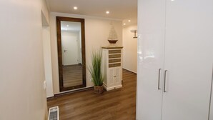 A hallway with wooden flooring, a white wardrobe, a white cabinet with drawers, a hanging plant, and a door leading to another room. - Island Feeling Apartment 2 (Büsum)