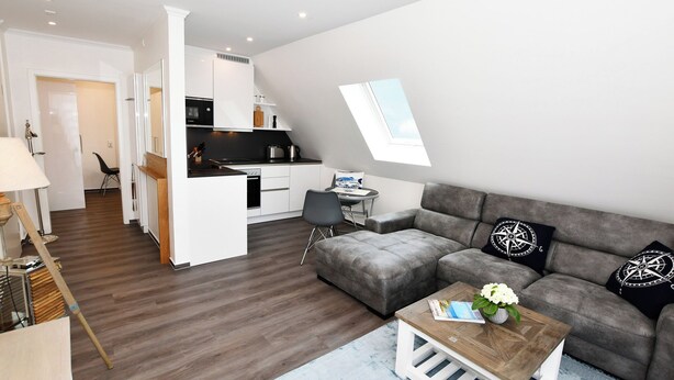 A modern living room with a grey sofa, a coffee table, and a dining area with a small table and chairs. - Island Feeling Apartment 3 (Büsum)