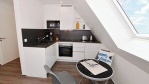 A compact kitchen with white cabinets, a black countertop, and a small dining area with a table and chair. - Island Feeling Apartment 3 (Büsum)