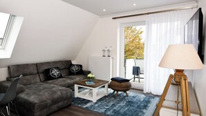 A modern living room with a sectional sofa, a coffee table, a lamp, and a view of the outdoors. - Island Feeling Apartment 3 (Büsum)