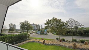 Blick von einem Balkon auf eine angelegte Grünfläche mit einer Straße, Bäumen und Gebäuden in der Ferne.