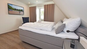 Ein modernes Hotelzimmer mit einem großen Bett, einem Schreibtisch mit Computer und Blick auf einen Park durch das Fenster.