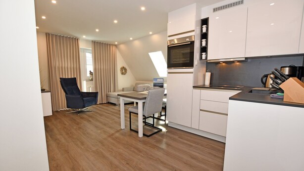 Een moderne keuken met witte kasten, een inbouwoven en een eethoek met een tafel en stoelen.