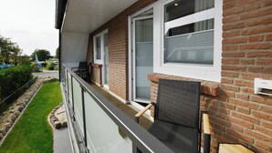 Een balkon met een zwart hekwerk, een bakstenen muur en een raam met luiken.