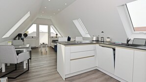 Et moderne køkken med hvide skabe, et spiseområde med et gråt bord og stole, samt en stor ovenlysvindue.