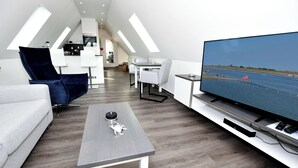 En moderne stue med et fladskærms-tv, et gråt sofabord og en blå lænestol.