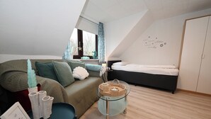 A modern, well-lit room with a loft bed, a glass coffee table, and a cozy seating area with cushions. - Noah's Ark - House by the sea<br>Apartment Sea (Büsum)