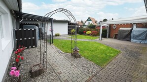 Een achtertuin met een geplaveid terras, een kleine bloementuin en een metalen toegangspoort.