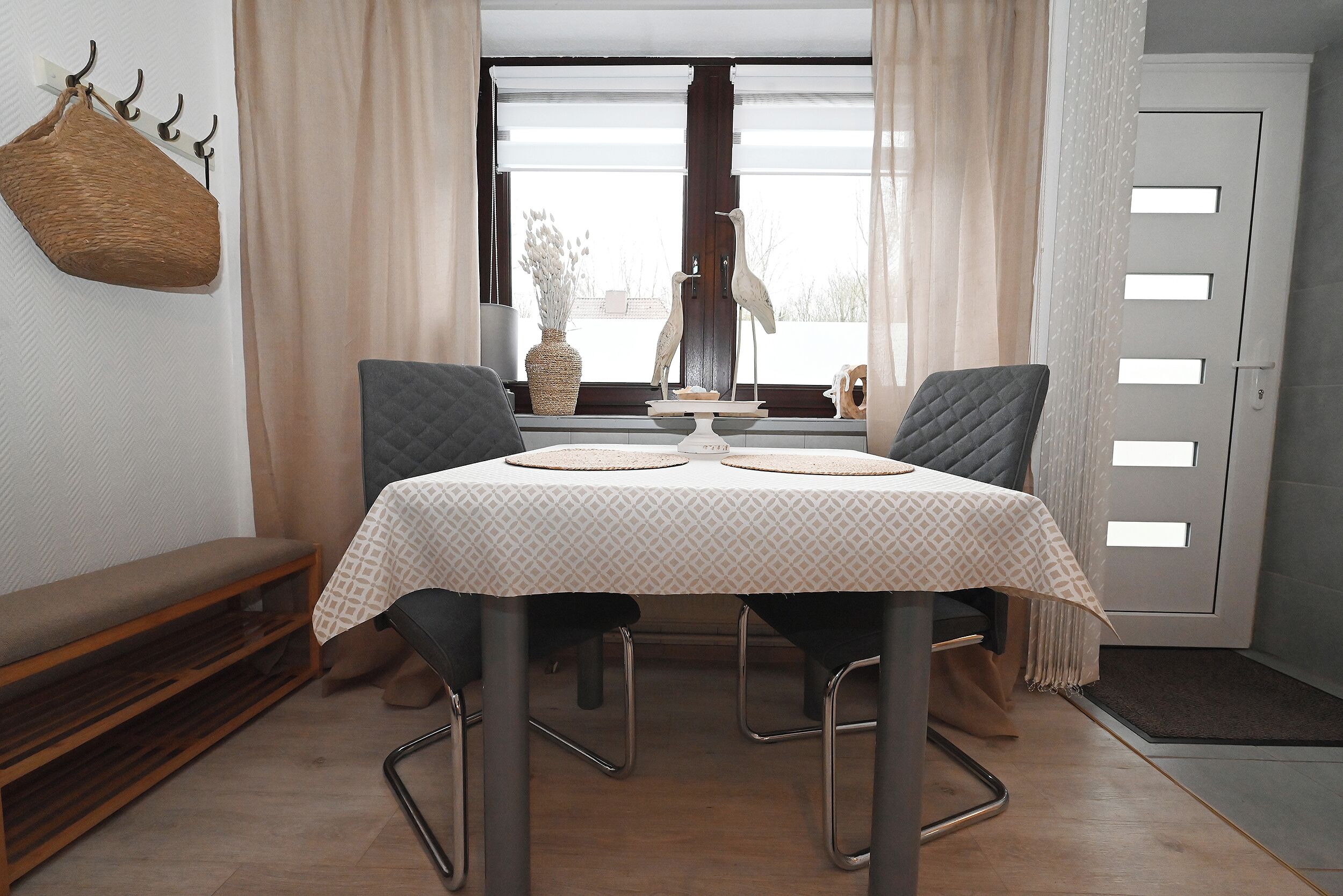 Uma área de refeições com uma mesa posta para dois, um banco e uma escultura decorativa de um pássaro.