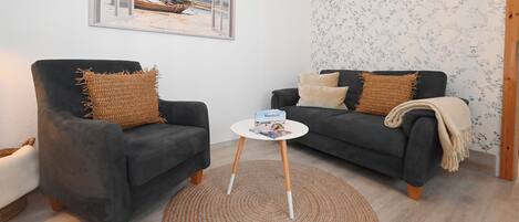A living room with two dark sofas, a small round coffee table, a woven rug, and a framed picture on the wall.