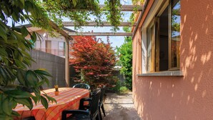 Un patio con mesa y sillas, una pérgola de madera y un árbol de hojas rojas.