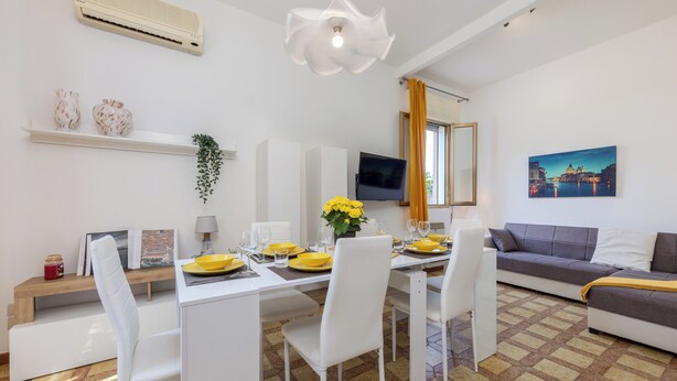 Una sala de estar moderna con zona de comedor, que incluye un sofá, un televisor y un cuadro de un paisaje urbano.