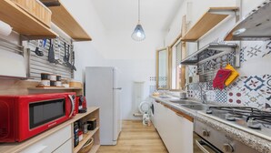 Una cocina compacta con un microondas rojo, un refrigerador blanco, una estufa y una lámpara colgante.