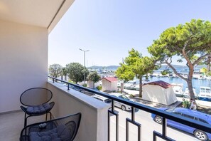 A balcony with a chair, a table, a view of a marina with boats, and a tree.