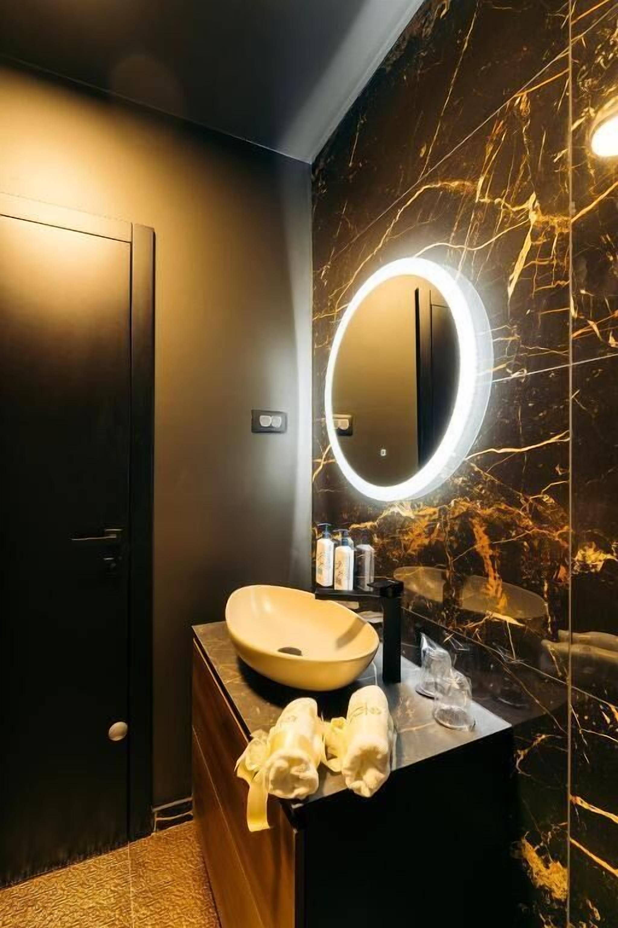 Un bagno moderno con uno specchio rotondo, un lavabo beige e una parete in marmo.