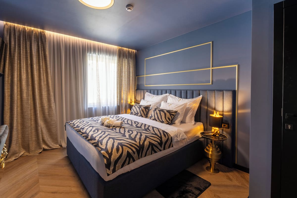 Ein Schlafzimmer mit Bett, Vorhängen, einem Nachttisch mit Lampe und einer Wandleuchte.