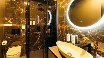 A modern bathroom with a marble wall, a round mirror, a toilet, and a sink with a vessel basin.