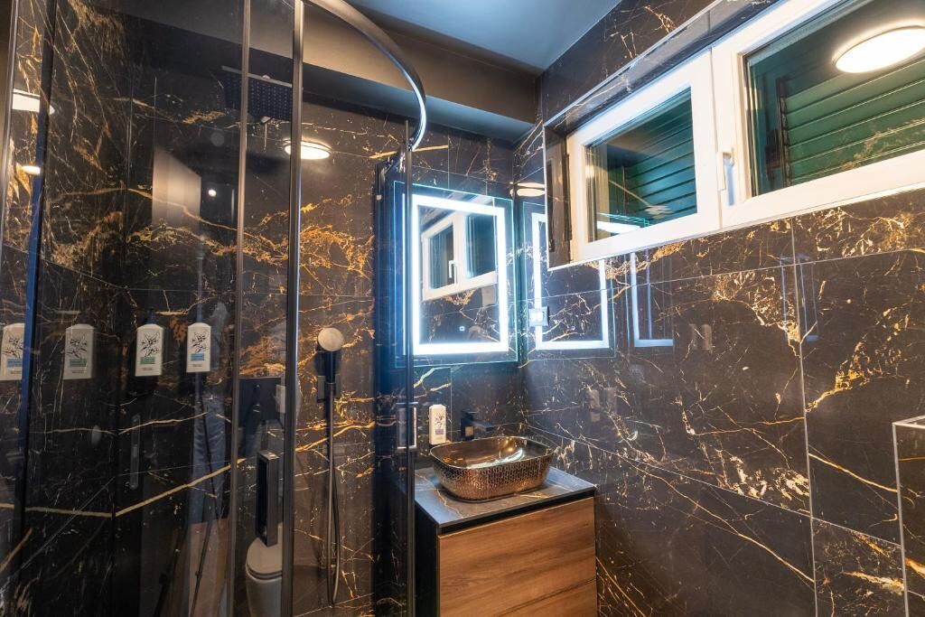 Ein modernes Badezimmer mit Marmorboden, einer Duschkabine aus Glas, einem Holzanbau und einem Spiegel mit beleuchtetem Rand.