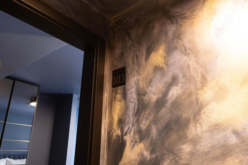 A room with a textured wall, a number sign, and a partial view of a bed.