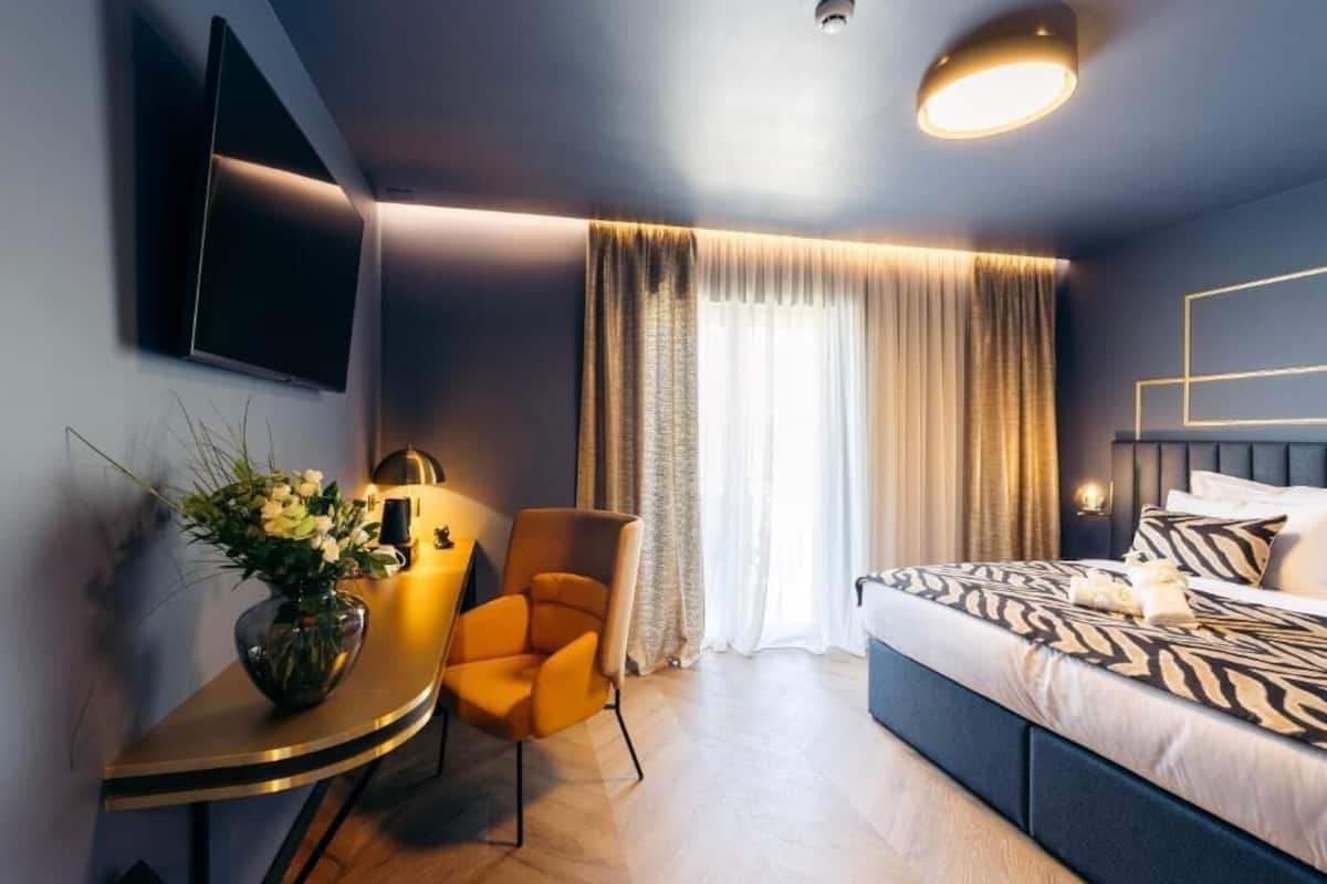 Ein modernes Hotelzimmer mit Bett, Schreibtisch mit Stuhl, Wand-Fernseher und einem Fenster mit Vorhängen.