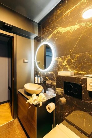 A modern bathroom with a marble wall, a round mirror, a sink, and a toilet. - Boutique Rooms Rogovo (Sveti Filip i Jakov)